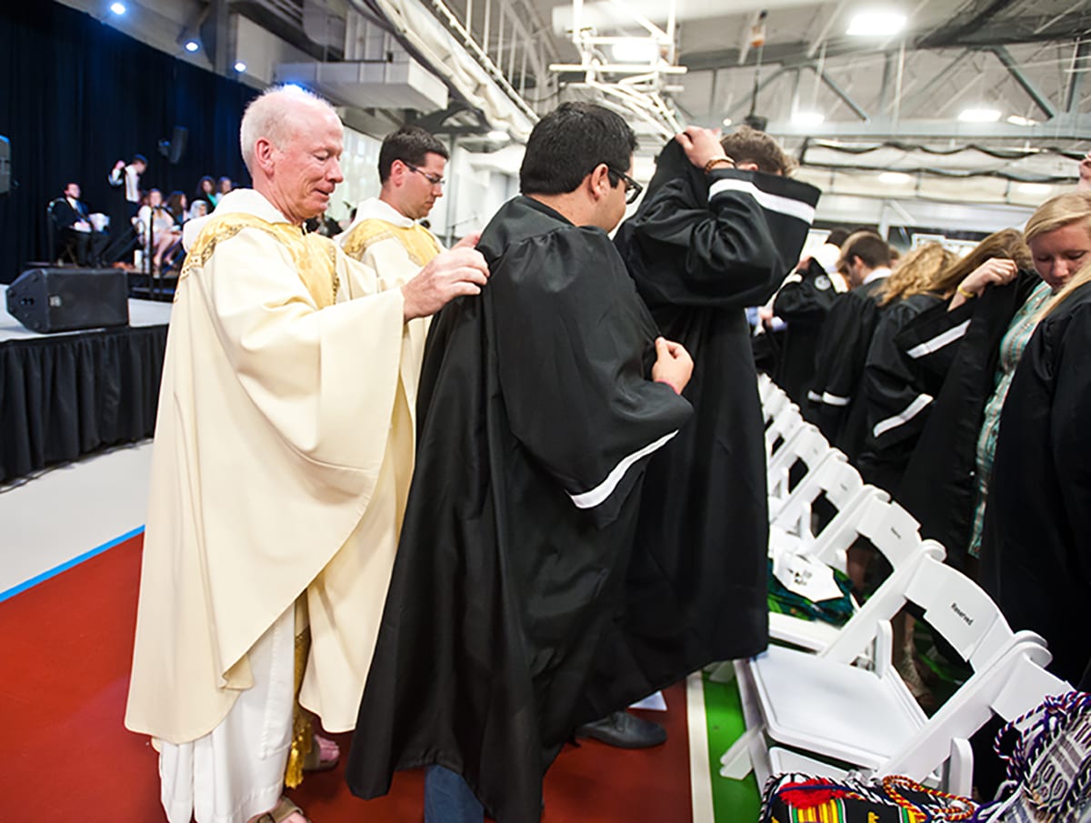 College President Rev. Brian J. Shanley, O.P. '80 assists Pedro Aleman '17 with his robe during the Service of Investiture ceremony of the Commencement Mass.