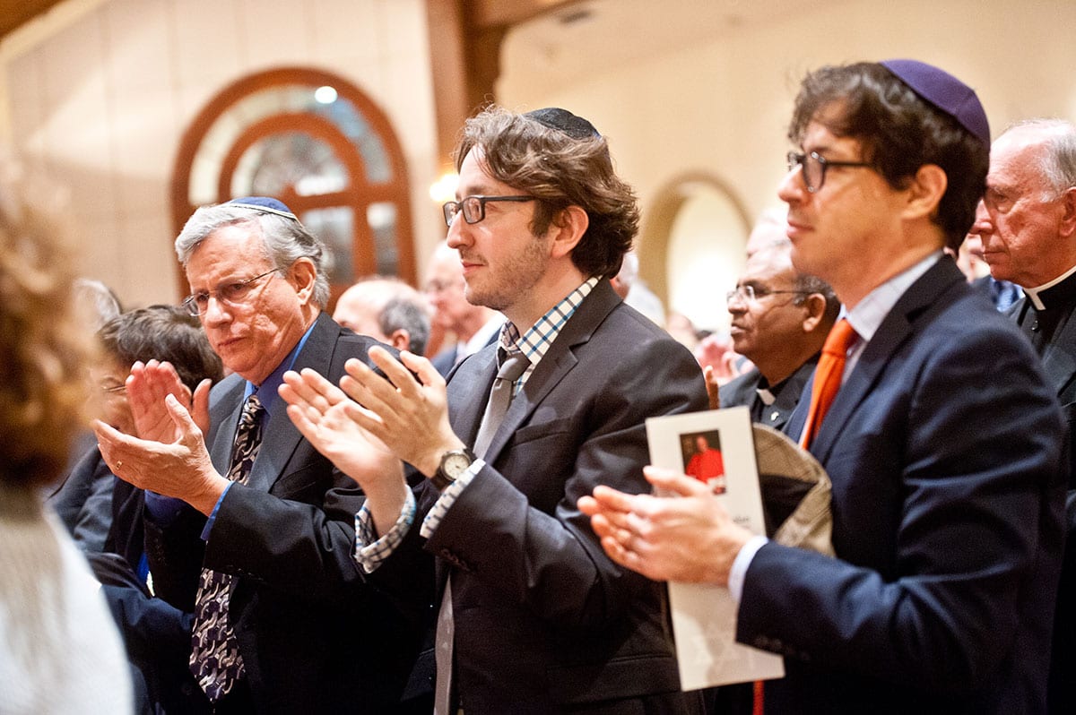 Dr. James S. Waters, center, assistant professor of biology and a member of the Jewish-Catholic Theological Exchange Committee, applauds Cardinal Dolan. 