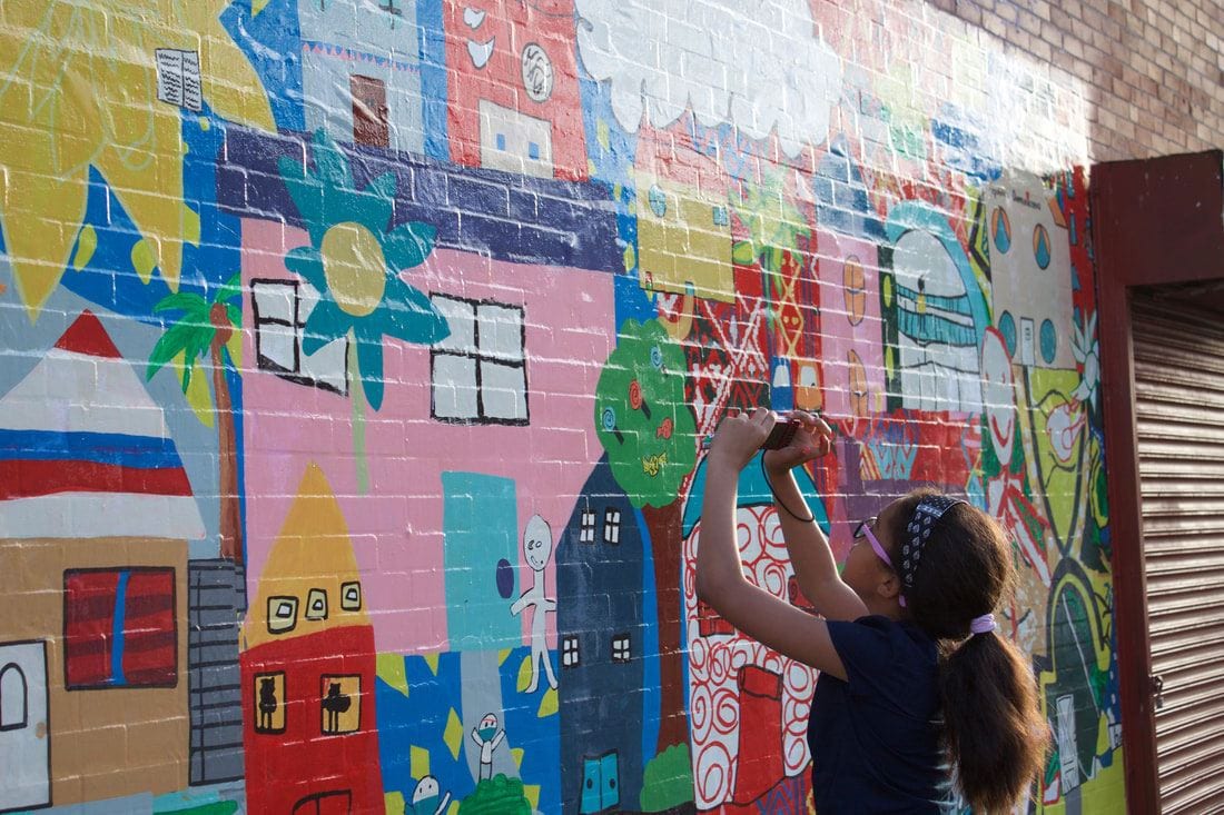 A young artist practices her photography skills by taking a photo of a mural outside the Providence CityArts for Youth center. She is being mentored by PC students in the Community Lens course. Photo by Elizabeth Longo '21.