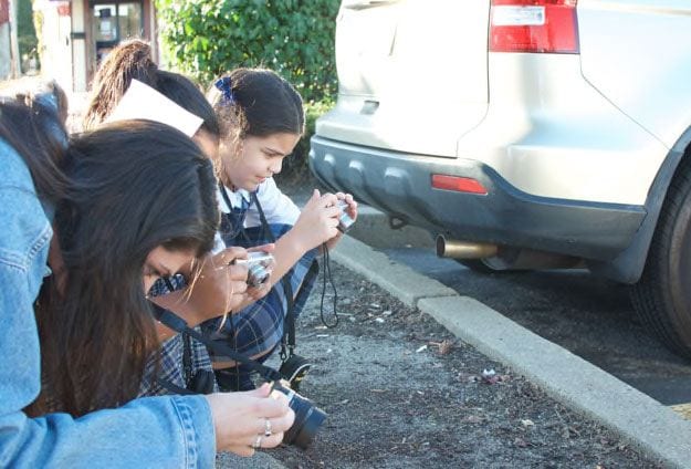 Kristen Lawler '18, left, shows two young artists how to zoom in and focus their cameras outside the Mount Pleasant Library. Photo by Payton Morse '20