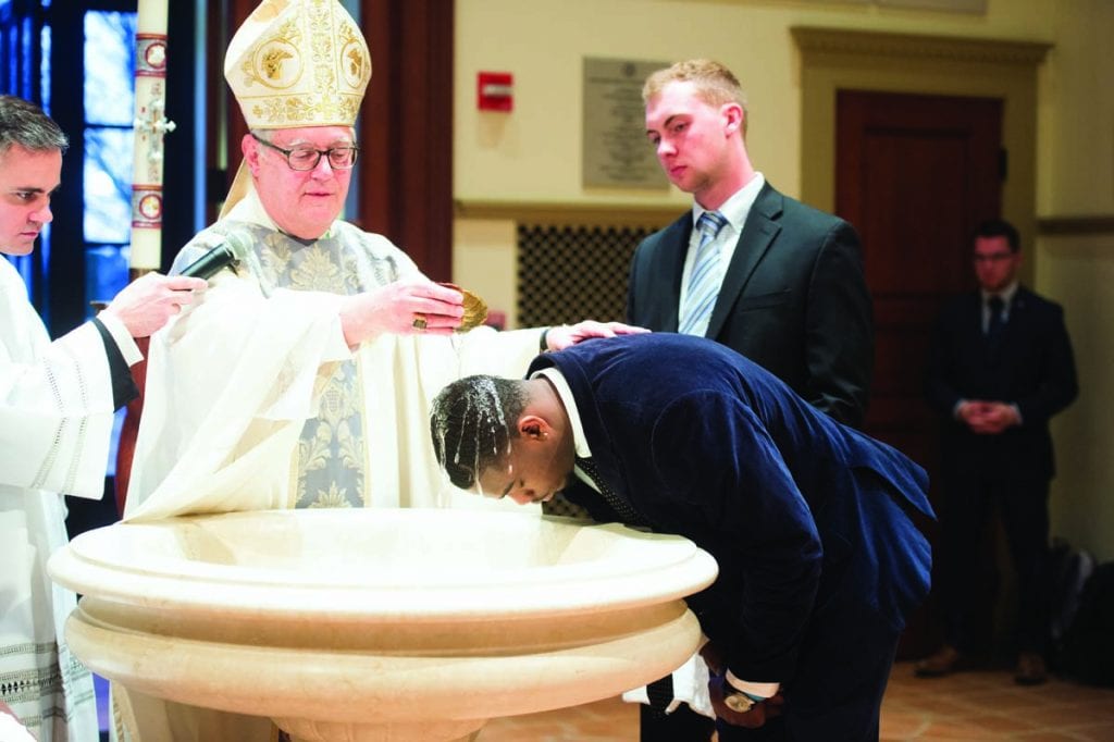 Most Rev. Thomas J. Tobin, D.D., bishop of Providence, baptizes Dinio Cijuste ’21 (South Orange, N.J.), a finance major and member of the lacrosse team. Cijuste’s coaches and teammates attended the Mass, including Ryan Poole '21 (Huntington, N.Y.), rear right, his sponsor. “It was amazing,” said Cijuste. “I felt like I rediscovered myself.”