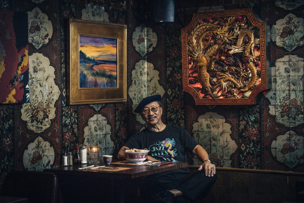 Wearing a shirt that advertises his restaurant as the home of jazz and blues, John Chan '74 poses in his restaurant dining room. One of his watercolor paintings is to his right.