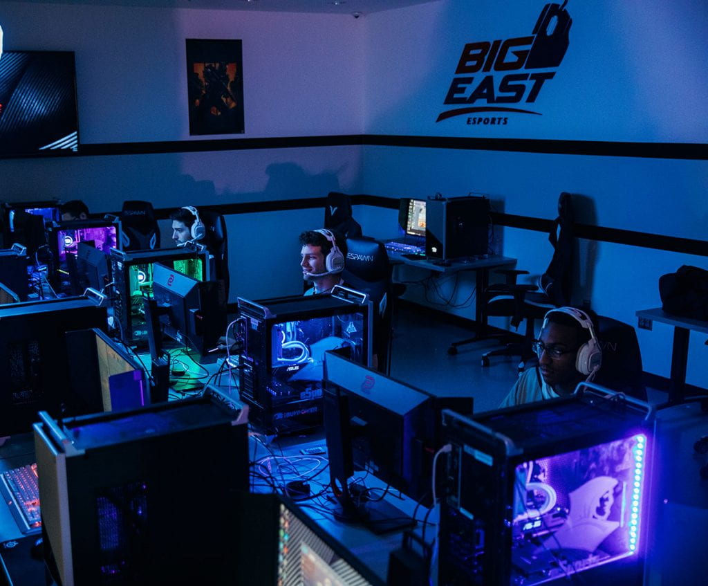 The BIG EAST logo looms over esports players, from left, Zachary Gandara '19, who is the graduate assistant for esports; Michael Fanelli '20, and Ahmad Mims '21.