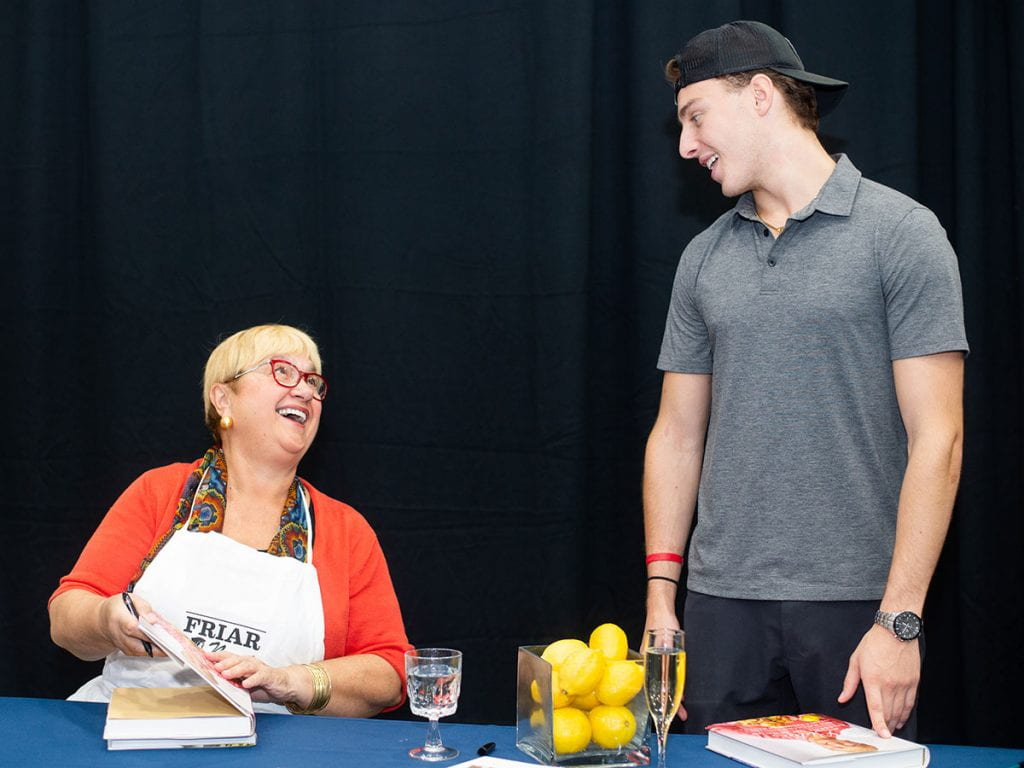 Lida Bastianich exchanges a smile with her grandson, Miles Bastianich '22, as she signs copies of her book. She is wearing an apron that reads, "Friar Nonni."