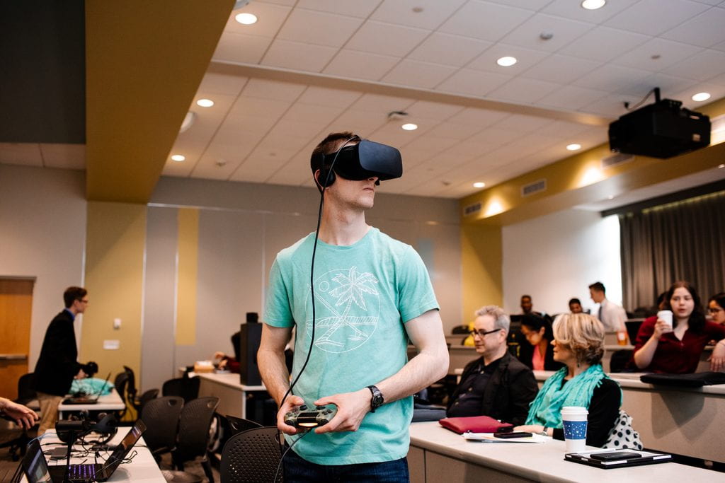 A student stands in a classroom wearing a VR headset in Asian Art Through VR Gaming.
