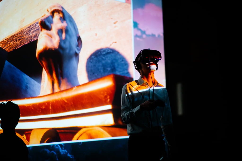 A student wearing a headset in the Asian Art through VR Gaming course examines European art, displayed on the screen behind him. ﻿