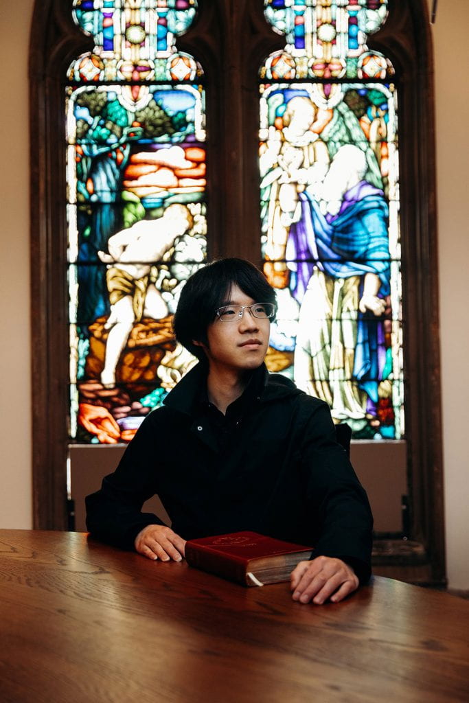 Tianyi Yuan '20 in the chapel of Guzman Hall with a stained glass window behind him.