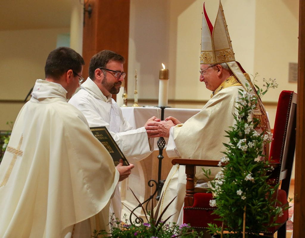 Brother Jordan Zajac, O.P. '04 kneels before Most Rev. Robert C. Evans, auxiliary bishop of Providence, and promises respect and obedience to the diocesan bishop and his religious superiors. Also pictured is Rev. Peter Martyr Yungwirth, O.P., College chaplain.