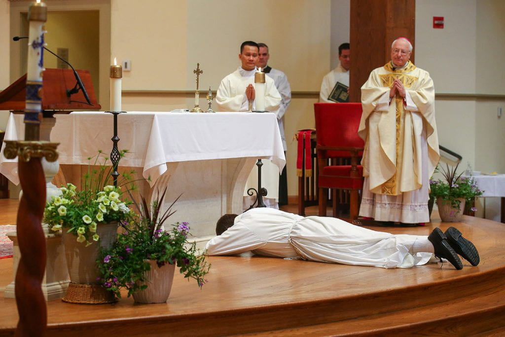 Brother Jordan Zajac, O.P. '04 lies prostrate before the altar in St. Dominic Chapel, symbolizing his unworthiness for the priesthood and his dependence upon God and the Christian community. Standing are Deacon Hiep Nguyen, a seminarian who was ordained a priest in the Diocese of Providence on June 6, and Most Rev. Robert C. Evans, auxiliary bishop of Providence.
