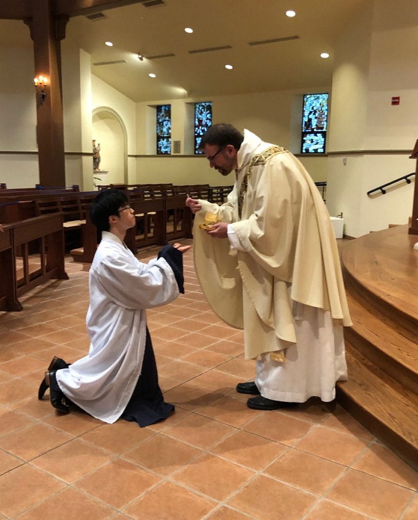 Tianyi Yuan '20 receives the Eucharist for the first time during an RCIA Mass in St. Dominic Chapel before beginning his studies at Harvard Divinity School. The priest is Rev. Jordan Zajac, O.P. '04.