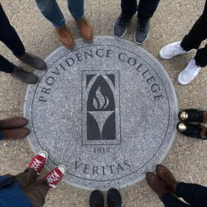 Students stand with their toes touching a granite circle printed with the PC logo and "Veritas."