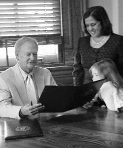 Rhode Island Gov. Lincoln D. Chafee looks over the commission he signed signifying Mary S. McElroy ’87 as the state public defender in 2012, as McElroy and her daughter, Chloe Jordan, look on.