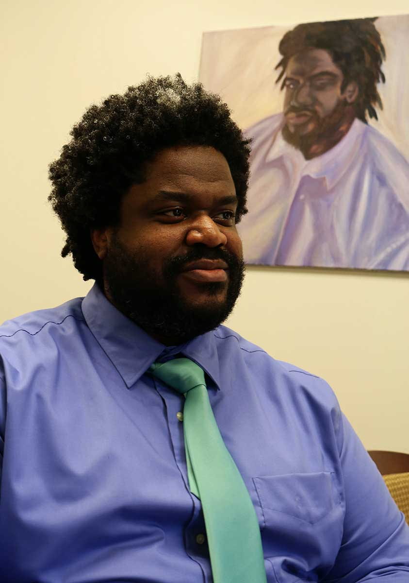 Nedzer Erilus '03, the new director of housing and residence life, poses in his office next to a portrait painted by a friend.