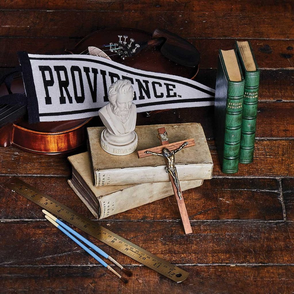 A Providence College pennant, a ruler, paint brushes, English books, a violin, a bust of Brahms, and a crucifix symbolizing themes studied in the Development of Western Civilization Program