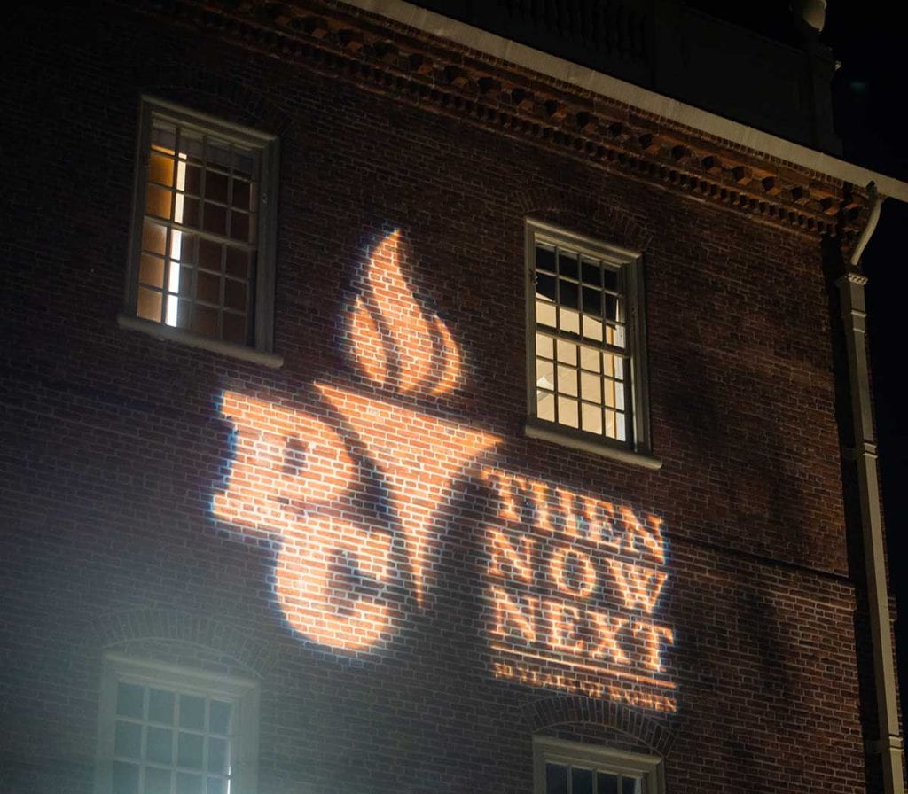 "Then Now Next," the logo for 50 Years of Women at Providence College, shines at WaterFire.