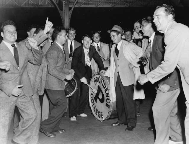 When Pearl Harbor was bombed on Dec. 7, 1941, football teammates at Providence College knew it was only a matter of time before they went to war. Here they have borrowed a drum from the band room to bid farewell to their teammate in the hat after marching him to the train station. The future Navy Lt. Cmdr. Joseph Vaghi Jr. '41 is third from right in the wire-rimmed eyeglasses.