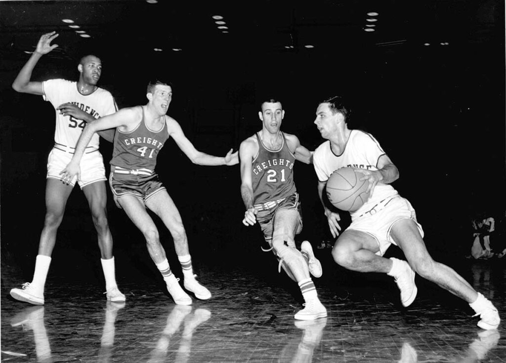 Johnny Egan '61, far right, drives to the basket in a game against Creighton. At left is Jim Hadnot '62.