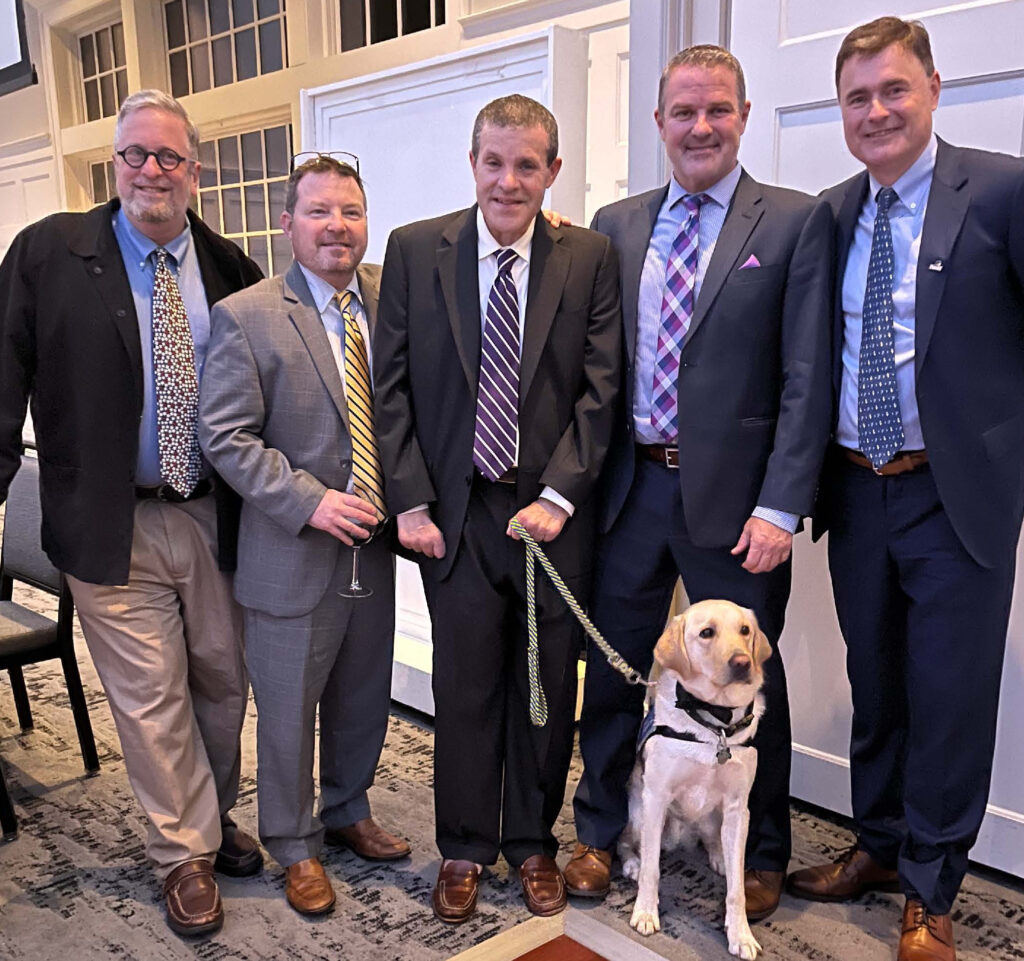 On hand to celebrate with John and his Canine Companions service dog, YoKen, were his friends from the fourth floor of Raymond Hall, from left, Jacques Lamarre ’90, Bill Coates ’90, Tom Whalen ’89, and Mark Jessup ’90.