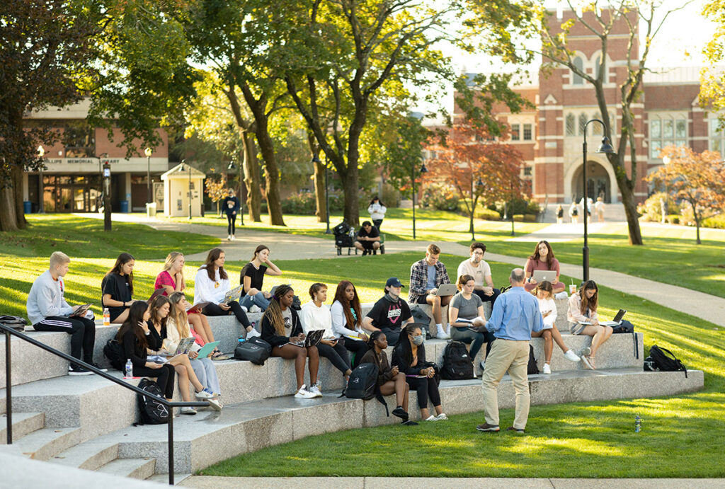 Robert Hackey, Ph.D., professor of health sciences, teaches an outdoor class with Phillips Memorial Library and the Ruane Center in the Humanities in the background.