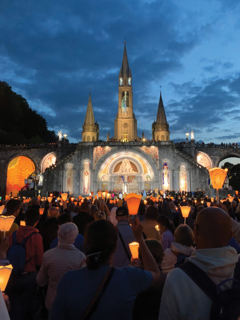 Thousands process by candlelight across the grounds of the Sanctuary of Our Lady of Lourdes, praying a multilingual rosary and singing Marian hymns.