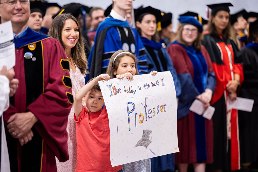 Mason and Vivi, the children of Saaid Mendoza, Ph.D., show their pride at Academic Convocation. Behind them is their mother, Jenny. They hold a sign reading "Our daddy is the best professor."