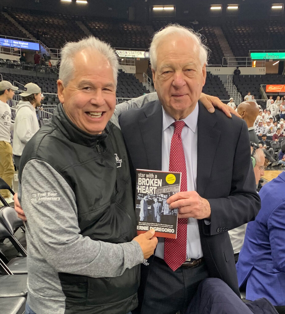 Ernie DiGregorio '73, left, displays a copy of his memoir alongside Bill Raftery, basketball analyst for Fox Sports, during a Friars game at Amica Mutual Pavilion in Providence.