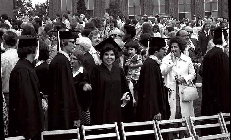 A female student in the midst of a crowd of graduates and spectators at the 1975 commencement.
