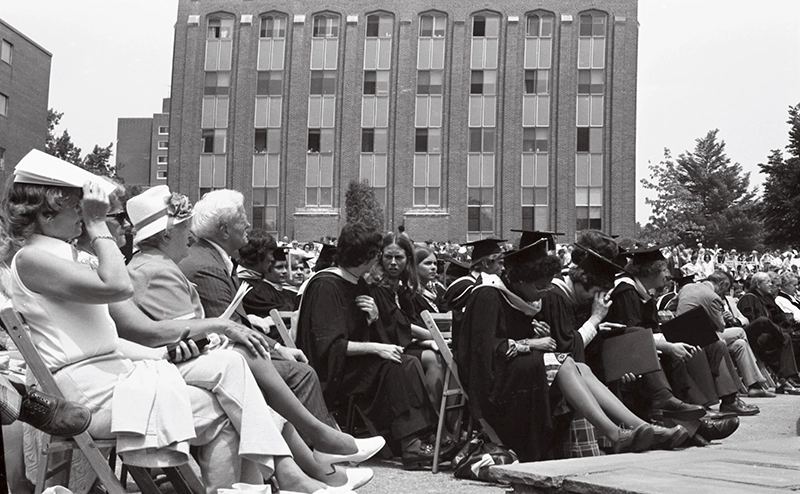 A woman shields her face with a commencement program on the hot commencement day in 1975.