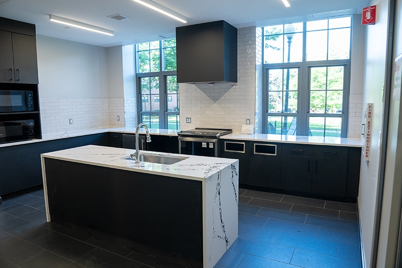 Black and white kitchen with island and sink, range, vent hood, countertops.