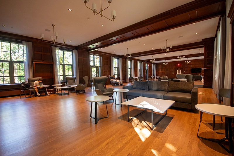 Large open room with wood floors, dark ceiling beams, couch, and cushioned chairs and tables