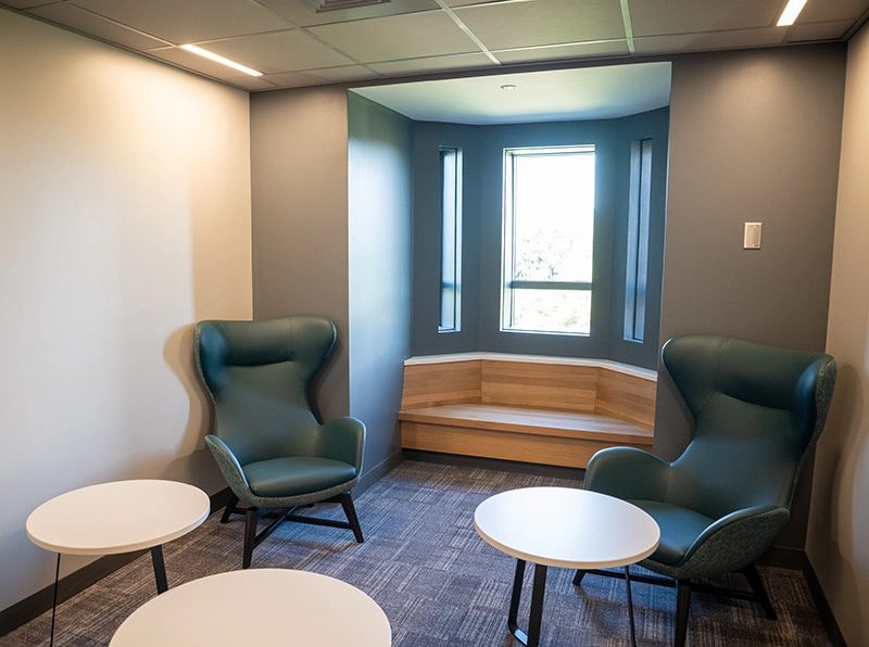 Cushioned chairs, small white tables, wooden bench in front of window nook