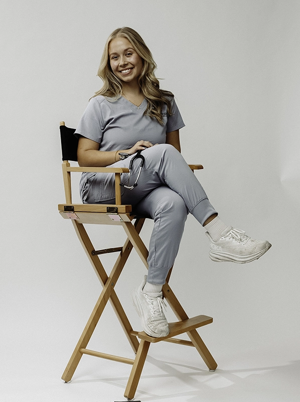 Aria Kriticos '27 sits in a director's chair wearing blue nursing scrubs.