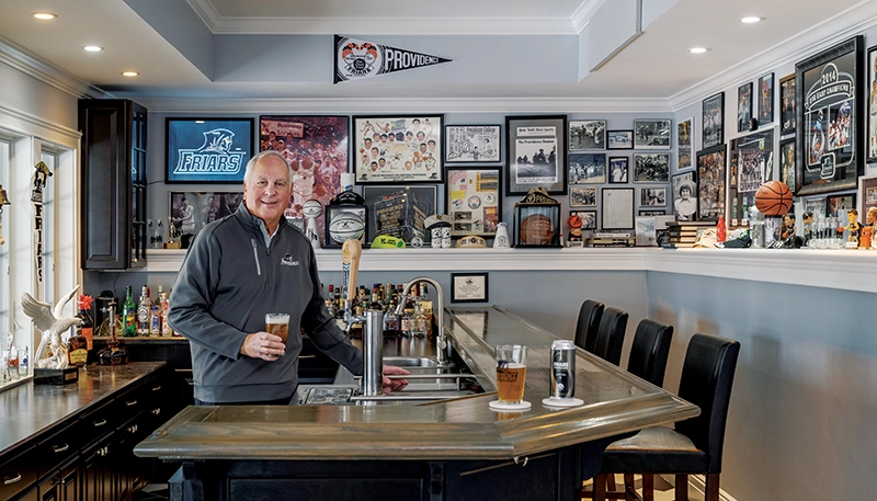 Chuck Borkoski in his Friar-themed bar surrounded by photos, memorabilia, posters, basketballs, and liquor bottles.