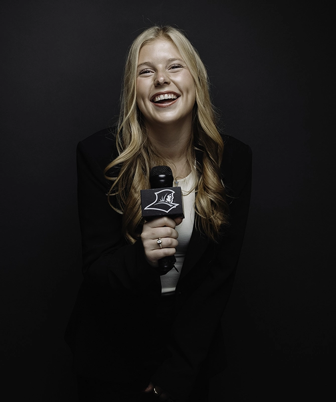 Caroline Austin '26 holds a microphone with the Friar head logo.