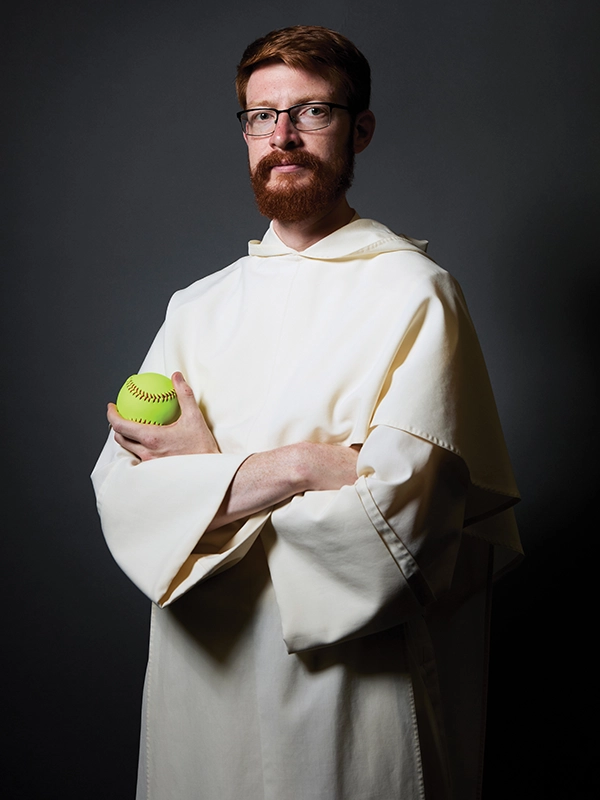A priest in a white robe holds a softball.
