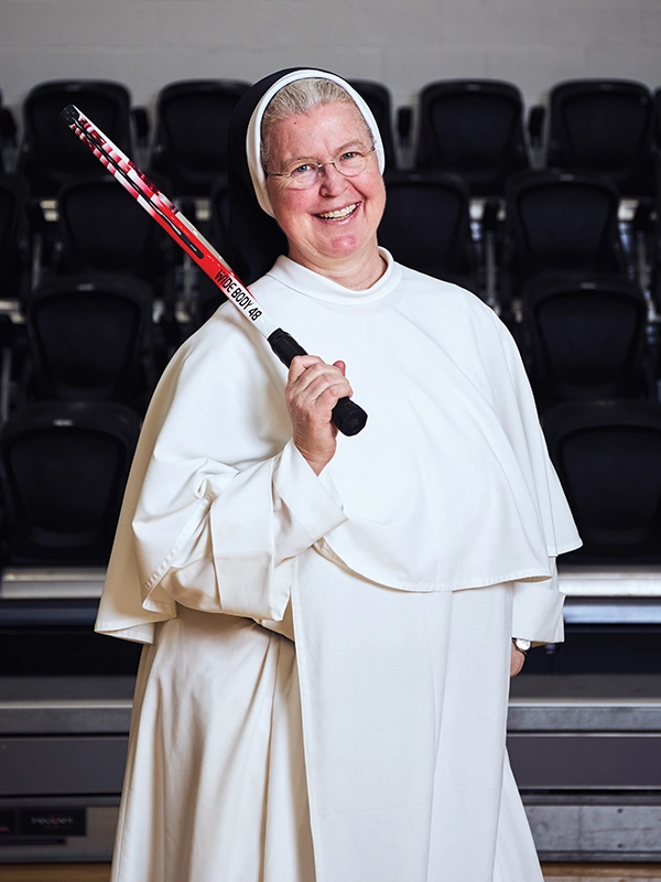 A religious sister in a white robe holds a tennis racket.