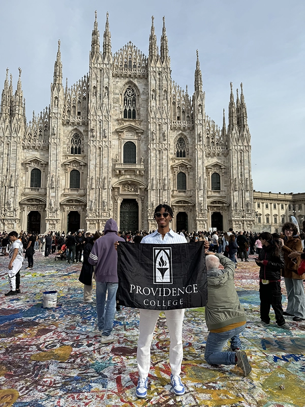 Daniel Singh '26 holds a Providence College flag outside a cathedral in Milan, Italy.
