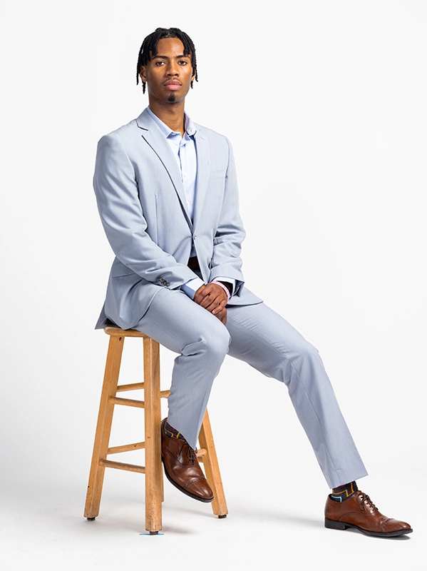 Daniel Singh '26 wears a blue suit and poses on a stool for a portrait.