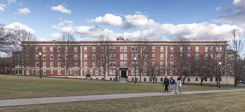 Fennell Hall, then a residence hall, as it looked in January 2023. Long brick building, students walking on a path.