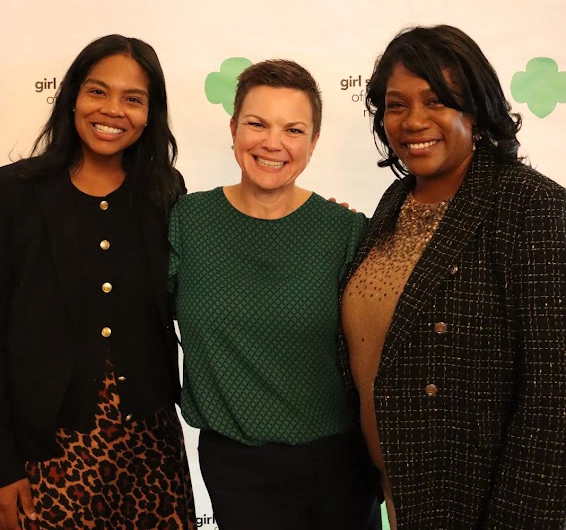 Three women stand in front of a Girl Scout banner.