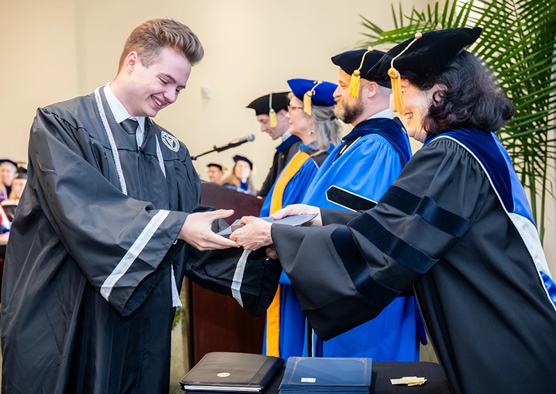 Leart Jahaj, wearing commencement robes, accepts a certificate from faculty members.