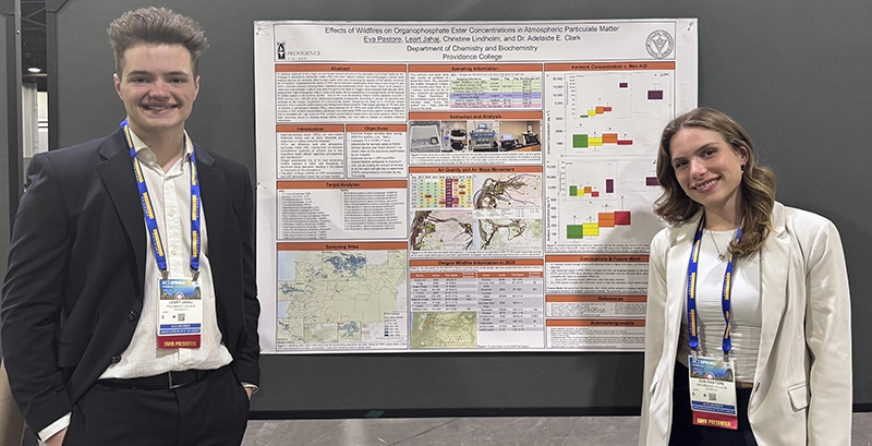 A male student and a female student stand in front of a research poster about particulate matter in wildfire smoke.