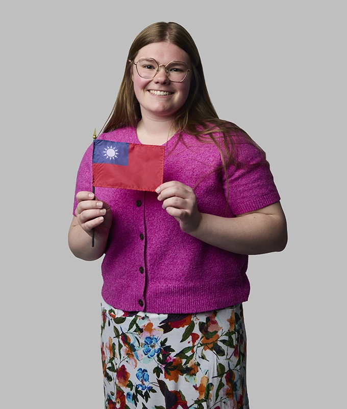 Female student holds a small Taiwanese flag while dressed in a pink sweater and floral skirt