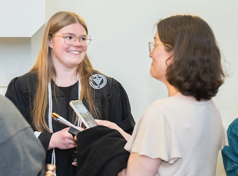 Student wearing graduation gown smiles at her mother