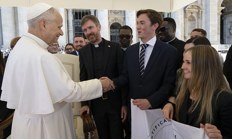 Pope Leo shakes hands with a Providence College student as other students and a priest look on.