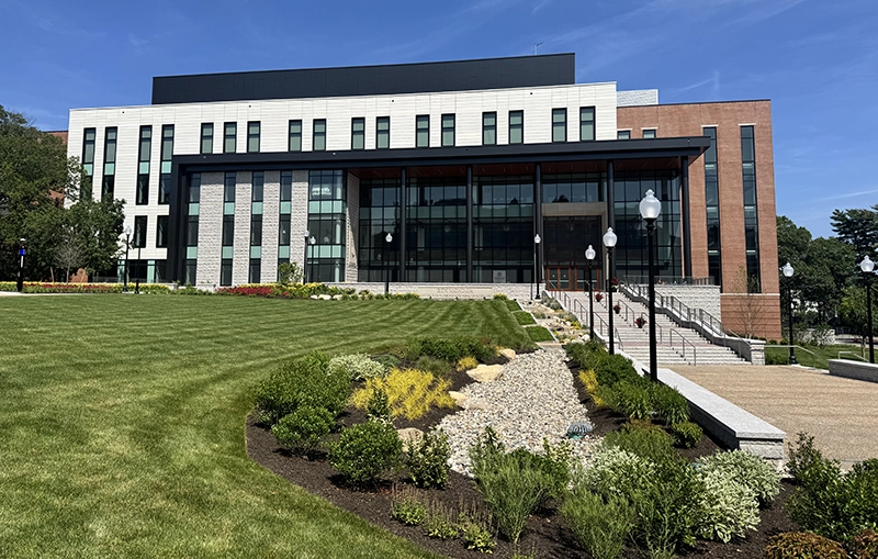 The Mondor Center for Nursing and Health Sciences as it looked in June 2025. It was built on the site Fennell Hall. Modern building with wide cement stairs, glass atrium, brick.