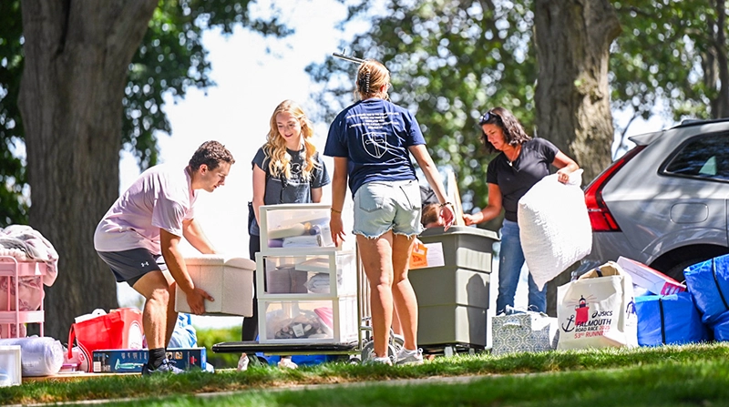 A mom and college-age students unpack bins and belongings from a vehicle on Move-In Day for the Class of 2029.