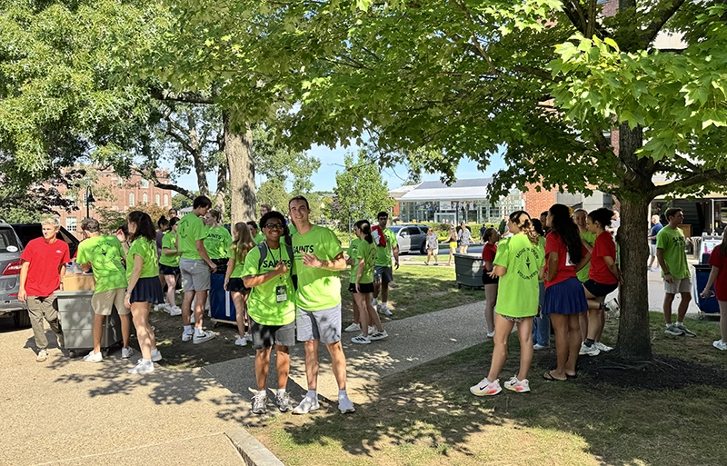 Student volunteers in yellow T-shirts stand about waiting to help students move into a residence hall.