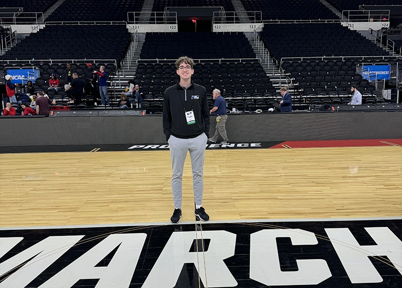 Nathan Cross '26 stands in the gym at Alumni Hall. "March Madness" is written on the floor.