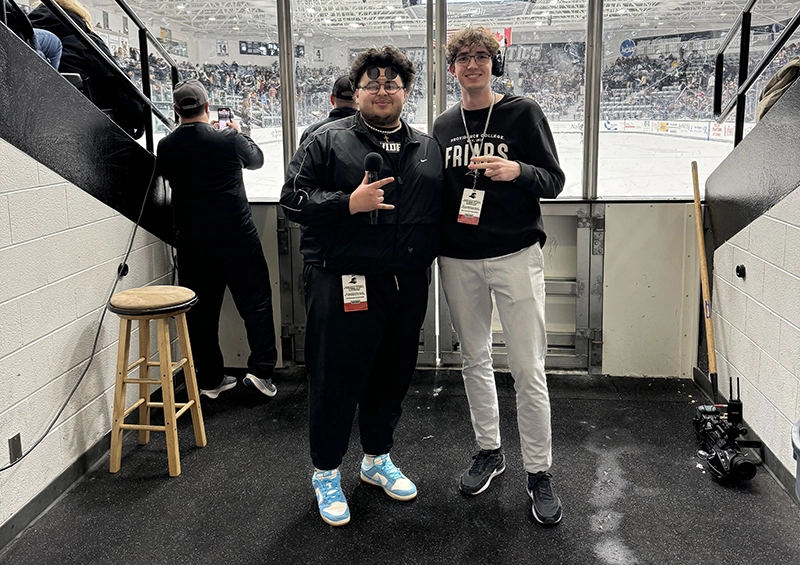 Nathan Cross '26 stands with Justin DeCosta, in-game host for PC Athletics, in the passage leading to the ice at Schneider Arena.